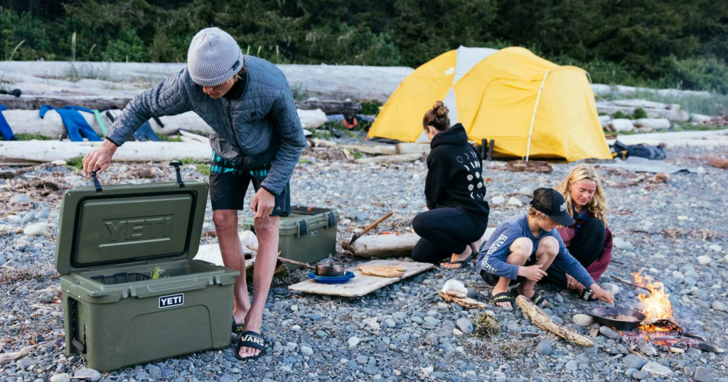  Friends sitting on a yeti cooler gray at a campsite showing its strength as modern outdoor gear.